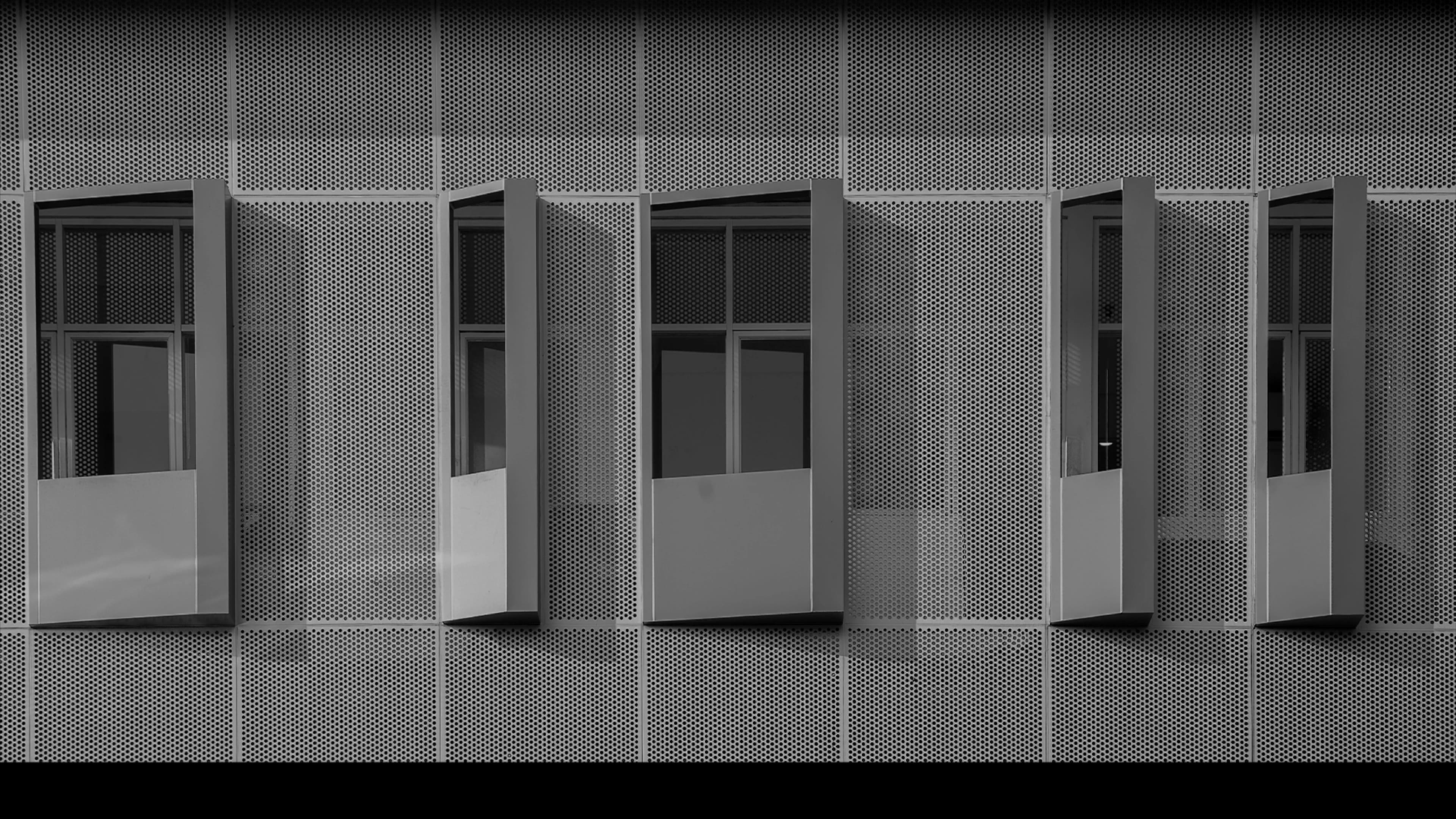 Windows with blue shutters in a perforated metal facade